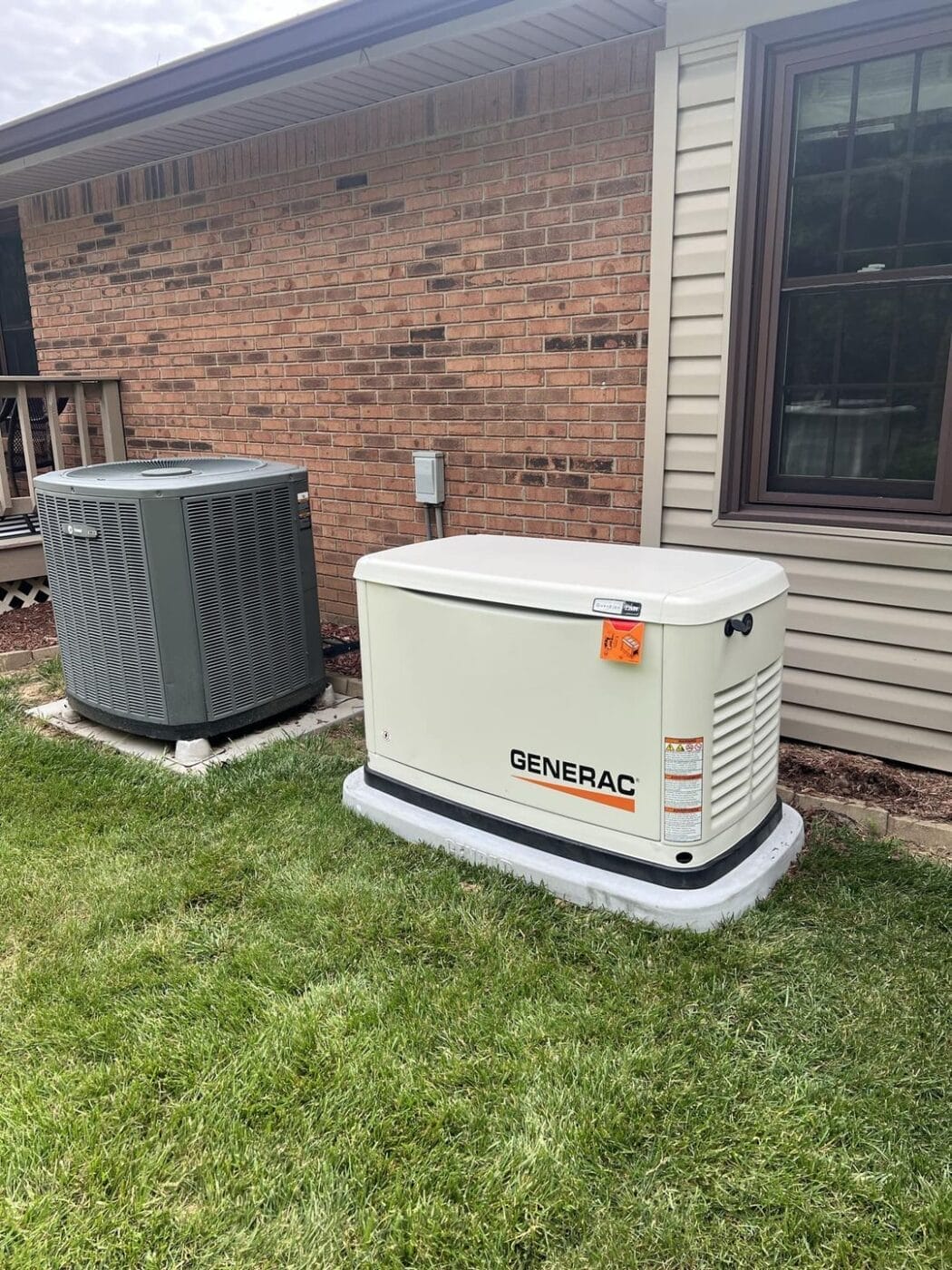 A Generac standby generator and an air conditioning unit are installed next to a brick house.